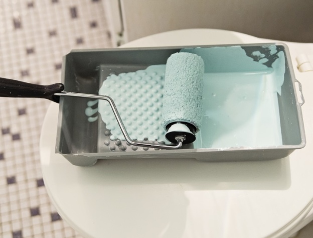 image of a closed toilet in a mosaic tiled bathroom with paint try and paint covered roller on top